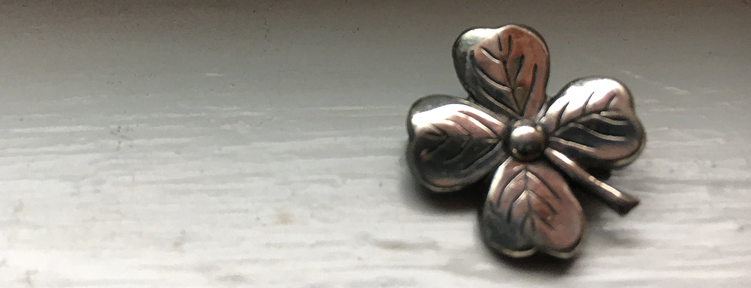 Vintage pewter shamrock pin sitting on a window sill